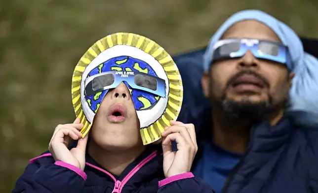 Dezaray Butts and her father Douglas wear solar eclipse glasses as they observe the partial phase of a total solar eclipse, in Kingston, Ontario, Monday, April 8, 2024. (Justin Tang/The Canadian Press via AP)