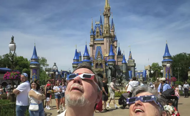 Maurice and Pat Moran from Rahway, New Jersey, watch the solar eclipse at the Magic Kingdom at Walt Disney World, in Lake Buena Vista, Fla., Monday, April 8, 2024. (Joe Burbank/Orlando Sentinel via AP)