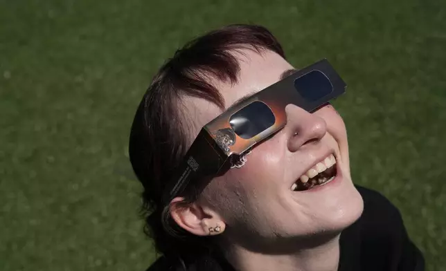 Jordan Elliott smiles as she watches with solar glasses as the moon starts to cross in front of the sun during a total solar eclipse Monday, April 8, 2024, in Carbondale, Ill. (AP Photo/Jeff Roberson)