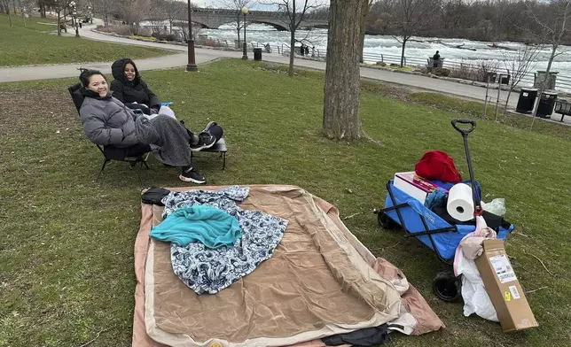 Synthia Nguyen and Jen Cerna from Washington, DC, claimed a prime spot on the lawn along the rapids in Niagara Falls State Park, to view the solar eclipse, Monday, April 8, 2024, in Niagara Falls, N.Y. (AP Photo/Carolyn Thompson)