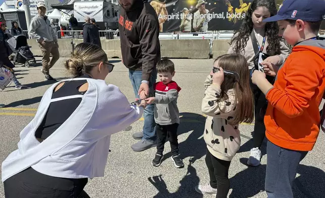 Volunteer Penelope Tsambounieris hands out eclipse special glasses to the Varouh family from Bay Village, Ohio, at the Great Lakes Science Center in Cleveland, on Sunday, April 7, 2024. (AP Photo/Stephanie Nano)