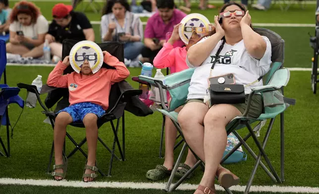 Karine Rodriquez, right, sits with her son Yurem, left, and daughter Aranza, center, as the moon partially covers the sun during a total solar eclipse, as seen from Eagle Pass, Texas, Monday, April 8, 2024. (AP Photo/Eric Gay)