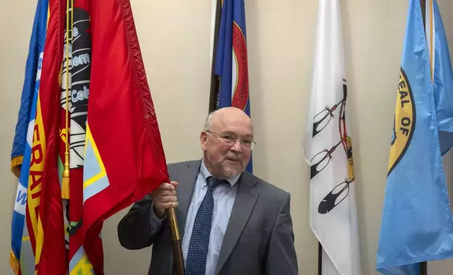 Tracy Toulou, the outgoing Director of the Office of Tribal Justice, holds the flag of the Colville Confederated Tribes, his tribal affiliation, alongside flags of tribal nations at the Department of Justice, Thursday, March 14, 2024, in Washington. For more than two decades, Toulou has confronted the serious public safety challenges facing Indian Country by working to expand the power of tribal justice systems. Today, tribal law enforcement finally has a seat at the table when federal authorities coordinate with state and local police, according to the Justice Department’s point person on Native American tribes. (AP Photo/Mark Schiefelbein)