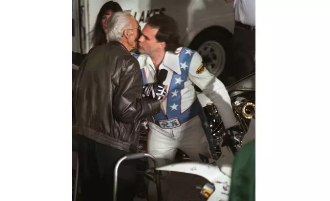 FILE - Robbie Knievel, right, kisses his daredevil father, Evel, before successfully jumping over 30 limousines on his motorcycle at the Tropicana Hotel in Las Vegas on Tuesday night, Feb. 24, 1998. (AP Photo/Jeff Scheid, File)