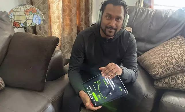 In this photo provided by Richard Persaud, he holds a tablet showing the stock chart of Trump Media &amp; Technology, at his home in Schenectady, N.Y., on Wednesday, April 24, 2024. “I don’t know which direction the stock is going,” says Persaud while checking his iPhone amid a recent surge. “It’s so unbelievably overvalued.” (Courtesy Richard Persaud via AP)