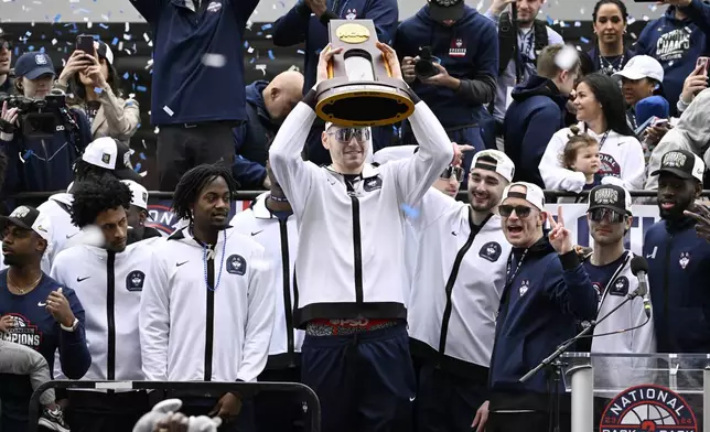 UConn's Donovan Clingan holds up the championship trophy as he stands with coaches and teammates during a parade to celebrate the team's NCAA college basketball championship, Saturday, April 13, 2024, in Hartford, Conn. (AP Photo/Jessica Hill)