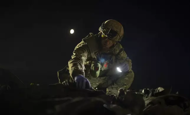 Oleksii Yukov examines the body of a Russian soldier he collected on the frontline in the Sloviansk region, Ukraine, Tuesday, Oct. 24, 2023. The 38-year-old martial arts instructor leads a team of volunteer body collectors in Ukraine. (AP Photo/Bram Janssen)