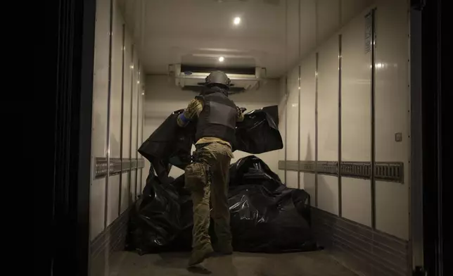 A member of Oleksii Yukov's body collector team piles the bodies of deceased Russians in a refrigerated truck in the Sloviansk region, Ukraine, Tuesday, Oct. 24, 2023. They retrieve bodies from the frontline to barter for Ukrainian bodies in periodic exchanges of war dead. (AP Photo/Bram Janssen)