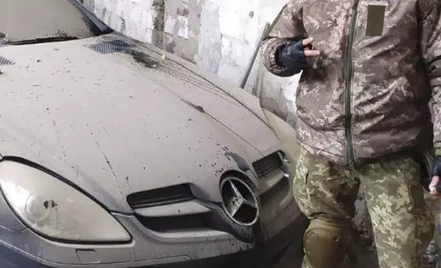 In this photo provided by his family, Oleksandr “Sasha” Romanovych Hrysiuk, in uniform, poses next to a luxury automobile in Ukraine. Soldiers from Sasha's unit said they were very sorry they couldn't take his body with them, the shelling was too heavy, all they could do was hide him in a cellar in Dovhenke – a rural settlement in eastern Ukraine that fell to the Russians. (Courtesy Olha Hrysiuk via AP)