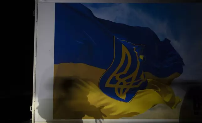 Oleksii Yukov, a Ukrainian volunteer body collector, casts a shadow over a refrigerated truck decorated with the Ukrainian flag in Sloviansk region, Ukraine, Tuesday, Oct. 24, 2023. The 38-year-old martial arts instructor says he's collected over 1,000 bodies since the full-scale invasion began two years ago, more than 580 of them Russians. (AP Photo/Bram Janssen)