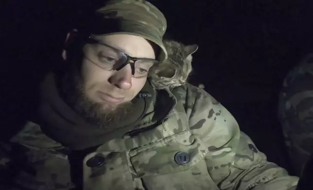 In this image from video provided by Platsdarm, a group of body collectors led by Oleksii Yukov, a kitten nuzzles Yukov in Dovhenke, Ukraine in November 2022, during a search for Oleksandr “Sasha” Romanovych Hrysiuk. The cat circled one spot in the wreckage. "Souls come over and wander next to us," Yukov explained. "A sign came to show us where he was lying... He wants to be back home. Mother is waiting." (Platsdarm via AP)