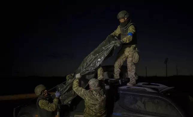 Oleksii Yukov's team members offload the bodies of Russian soldiers they've collected from the frontline in the Sloviansk region, Ukraine, Tuesday, Oct. 24, 2023. Yukov and his team retrieve bodies from the frontline to barter for Ukrainian bodies in periodic exchanges of war dead. (AP Photo/Bram Janssen)