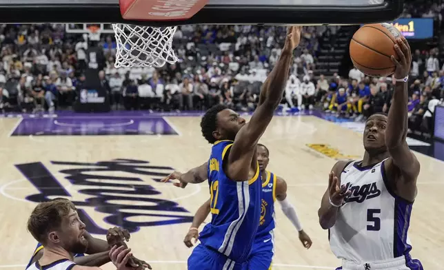 Sacramento Kings guard De'Aaron Fox (5) shoots while defended by Golden State Warriors forward Andrew Wiggins (22) during the second half of an NBA basketball play-in tournament game Tuesday, April 16, 2024, in Sacramento, Calif. (AP Photo/Godofredo A. Vásquez)