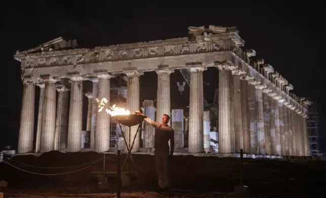 Retired Greek 400-meter hurdles champion Periklis Iakovakis lights a cauldron with the Olympic flame in front of the ancient Parthenon temple at the Acropolis hill, Friday, April 19, 2024. The flame that will burn at the summer Olympics is spending the night at the ancient Acropolis in Athens, a week before its handover to Paris 2024 organizers. (AP Photo/Petros Giannakouris)