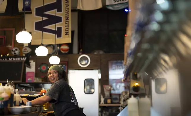 Bartender M.J. Jones looks to the drinks menu while serving a customer at The Sports Bra sports bar on Wednesday, April 24, 2024, in Portland, Ore. (AP Photo/Jenny Kane)