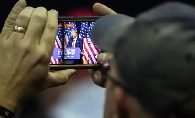 FILE - A supporter takes a photo as Republican presidential candidate former President Donald Trump speaks at a campaign rally Saturday, March 9, 2024, in Rome Ga. Phunware, a Texas-based company, built a cellphone app for Trump’s 2020 bid that allowed staff to monitor the movements of his millions of supporters and mobilize their social networks. Since then, Phunware obtained a patent for what a former company official described as “experiential AI” that can locate people’s cell phones geographically, predict their travel patterns and incentivize their consumer behavior. (AP Photo/Mike Stewart, File)