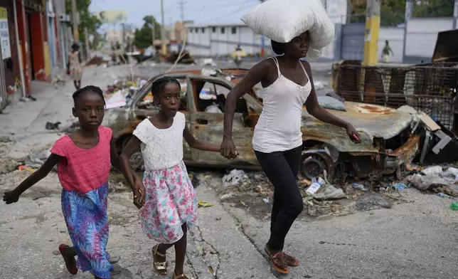 Residents walk past a burnt car blocking the street as they evacuate the Delmas 22 neighborhood the morning after an attack amid gang violence in Port-au-Prince, Haiti, Thursday, May 2, 2024. (AP Photo/Ramon Espinosa)