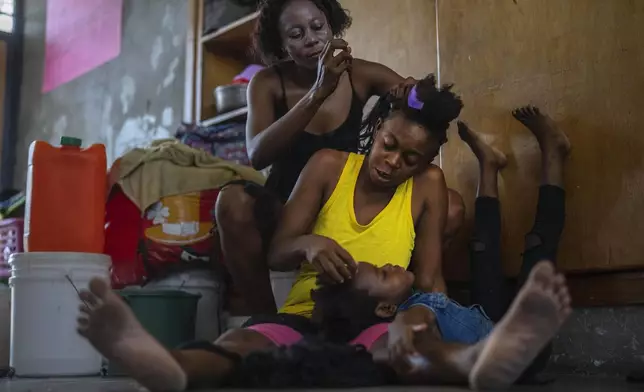 A child rests her head on the lap of her mother as she gets her hair done, at a school turned into a makeshift shelter for people displaced by gang violence, in Port-au-Prince, Haiti, Wednesday, May 8, 2024. (AP Photo/Ramon Espinosa)