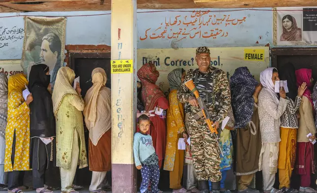 A paramilitary soldier stands guard as Kashmiri women queue up at a polling booth to cast their vote in the sixth round of polling in India's national election in Lidroo, south of Srinagar, Indian controlled Kashmir, Saturday, May 25, 2024. (AP Photo/Dar Yasin)