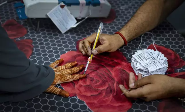 A voter with hennaed hands gets her finger marked with an indelible ink as she casts her vote in the sixth round of polling in India's national election in New Delhi, India, Saturday, May 25, 2024. (AP Photo/Altaf Qadri)