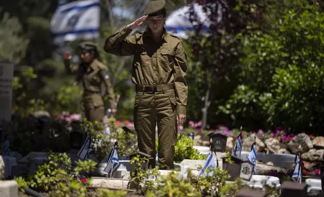 An Israeli soldier salutes after placing a flag with black ribbons on the grave of a soldier ahead of the country's memorial day for fallen soldiers at the Mount Herzl military cemetery in Jerusalem, Isreal, Wednesday, May 8, 2024. Israel marks the annual Memorial Day in remembrance of soldiers who died in the nation's conflicts. (AP Photo/Leo Correa)