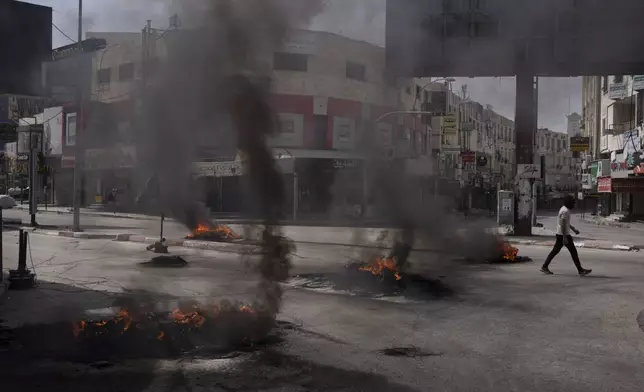 A Palestinian man walks past burning tires during clashes with Israeli forces in the West Bank city of Jenin, Wednesday, May 22, 2024. (AP Photo/Leo Correa)
