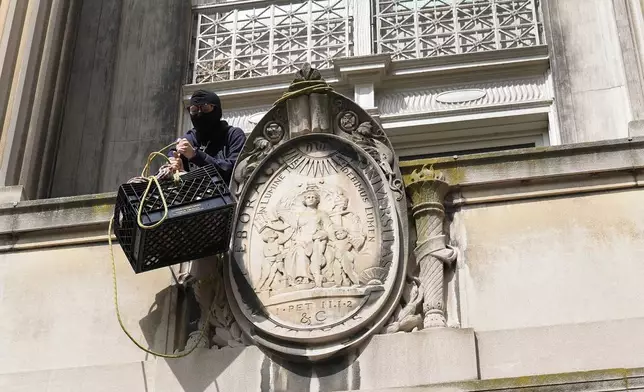 A student protester pulls up a crate filled with food and supplies from a balcony of Hamilton Hall on the campus of Columbia University, Tuesday, April 30, 2024, in New York. Early Tuesday, dozens of protesters took over Hamilton Hall, locking arms and carrying furniture and metal barricades to the building. Columbia responded by restricting access to campus. (AP Photo/Mary Altaffer, Pool)