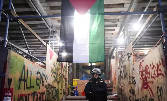 A police officer stands under a Palestinian flag after a raid on an encampment on the UCLA campus Thursday, May 2, 2024, in Los Angeles. (AP Photo/Jae C. Hong)