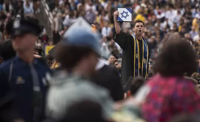A graduate holds his cap with an Israeli flag while shouting at pro-Palestinian protesters as they demonstrate during the University of Michigan's Spring 2024 Commencement Ceremony at Michigan Stadium in Ann Arbor, Mich., Saturday, May 4, 2024. (Katy Kildee/Detroit News via AP)