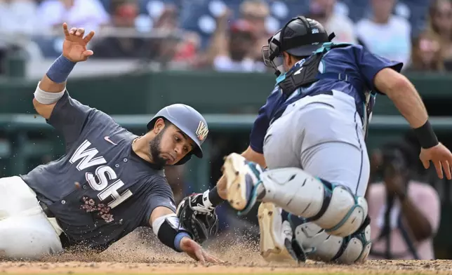 Washington Nationals' Keibert Ruiz, left, beats the tag of Seattle Mariners catcher Cal Raleigh at home plate during the seventh inning of a baseball game, Saturday, May 25, 2024, in Washington. (AP Photo/John McDonnell)