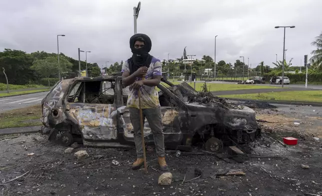 A man stands in front a burnt car after unrest in Noumea, New Caledonia, Wednesday May 15, 2024. France has imposed a state of emergency in the French Pacific territory of New Caledonia. The measures imposed on Wednesday for at least 12 days boost security forces' powers to quell deadly unrest that has left four people dead, erupting after protests over voting reforms. (AP Photo/Nicolas Job)