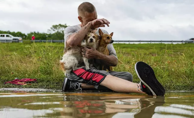Tim McCanon sits on the road with his dogs after being rescued by the Community Fire Department during severe flooding on Friday, May 3, 2024, in New Caney, Texas. (Raquel Natalicchio/Houston Chronicle via AP)
