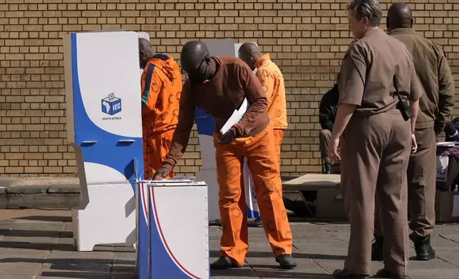 An officer watches on as an inmate inserts his ballot paper into the ballot box at the polling station at Kgoši Mampuru Correctional Facility in Pretoria, South Africa, Wednesday, May 29, 2024. South Africans voted Wednesday at schools, community centers, and in large white tents set up in open fields in an election seen as their country’s most important in 30 years. It could put the young democracy in unknown territory. (AP Photo/Themba Hadebe)