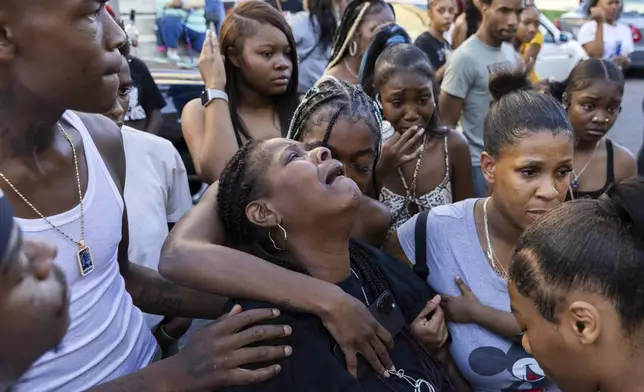 Friends and family comfort Antonio Lee's mother as she mourns her son at a vigil, Friday, Aug. 18, 2023, in Baltimore. Lee, 19, was shot and killed while squeegeeing in Baltimore. Two kids named Antonio grew up together in the streets of east Baltimore surrounded by poverty and gun violence. But only one would make it out alive. Antonio Moore is a successful real estate investor and marketing consultant. His friend Antonio Lee was shot and killed last summer, four months before his 20th birthday. (AP Photo/Julia Nikhinson)