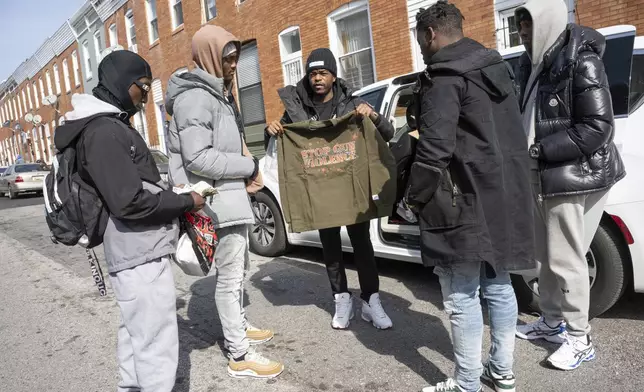 Antonio Moore, center, 24, of Baltimore, hands out designer t-shirts reading "Stop Gun Violence" in his childhood neighborhood in east Baltimore, Monday, Feb. 26, 2024. Moore, is a successful real estate investor and entrepreneur who founded a consulting company that helps brands and nonprofits connect with urban youth. (AP Photo/Steve Ruark)