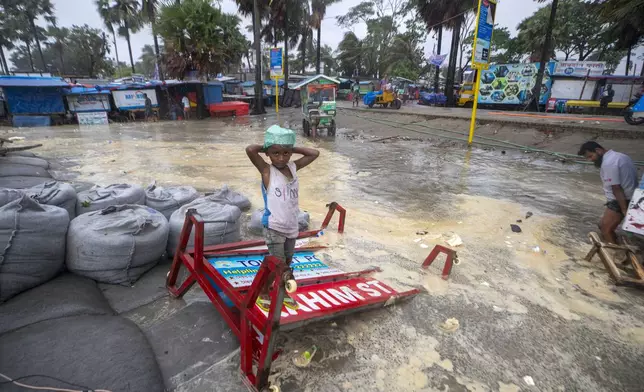 A boy stands on a broken signboard as water flows on to the Kuakata beach on the coast of Bay of Bengal caused by the advancing Cyclone Remal in Barisal, Bangladesh, Sunday, May 26, 2024. (AP Photo/Abdul Goni)