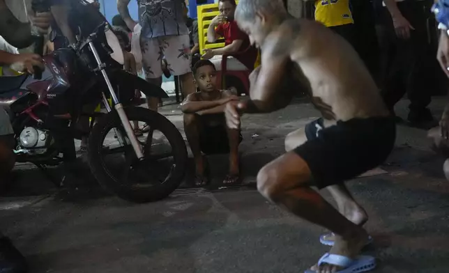 FILE - A boy watches youth perform the street dance style known as passinho in the Rocinha favela of Rio de Janeiro, Brazil, April 11, 2024. Passinho or "little step" began with small groups performing at parties inside Rio's favelas, but has since spread, helping to break the stigma of the communities often known for violence and drug gangs. (AP Photo/Silvia Izquierdo, File)