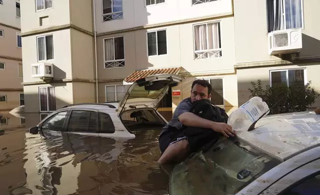 A man supports himself on a car as he tries to return to his flooded apartment building after heavy rain in Canoas, Rio Grande do Sul state, Brazil, Thursday, May 9, 2024. (AP Photo/Carlos Macedo)