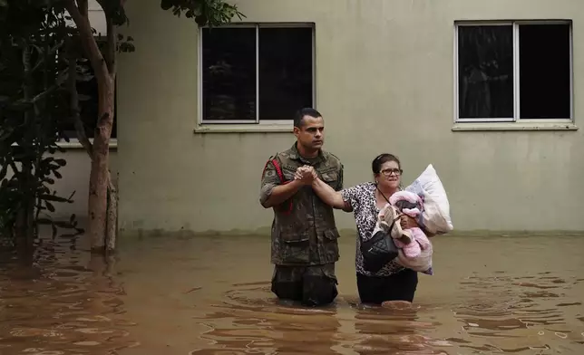A soldier helps a woman evacuate from a neighborhood flooded by heavy rains, in Canoas, Rio Grande do Sul state, Brazil, Saturday, May 4, 2024. (AP Photo/Carlos Macedo)