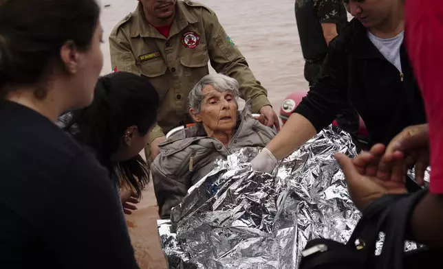 Firefighters and volunteers carry an elderly woman rescued from a flooded area after heavy rains in Porto Alegre, Rio Grande do Sul state, Brazil, Saturday, May 4, 2024. (AP Photo/Carlos Macedo)