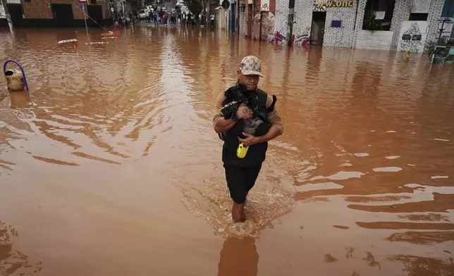 A man, cradling a dog, wades through a street flooded by heavy rains in Porto Alegre, Rio Grande do Sul state, Brazil, Saturday, May 4, 2024. (AP Photo/Carlos Macedo)