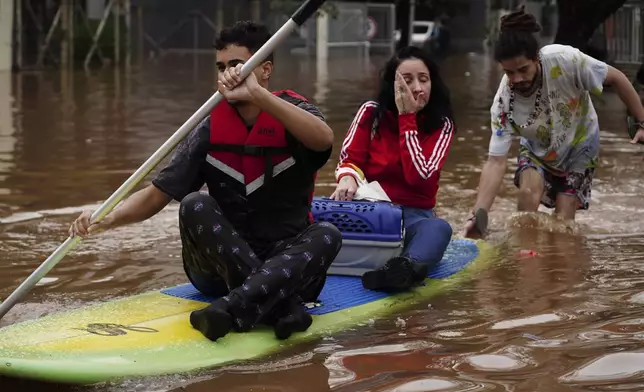People evacuate on a surfboard from a neighborhood flooded by heavy rains, in Canoas, Rio Grande do Sul state, Brazil, Saturday, May 4, 2024. (AP Photo/Carlos Macedo)