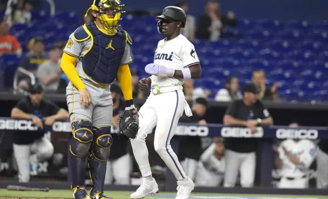 Miami Marlins' Jazz Chisholm Jr., right, scores on a RBI single hit by Otto Lopez during the second inning of a baseball game, Tuesday, May 21, 2024, in Miami. At left is Milwaukee Brewers catcher William Contreras. (AP Photo/Lynne Sladky)