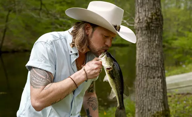Brian Kelley kisses a fish he caught from a pond outside his cabin Wednesday April 17, 2024, in Nashville, Tenn. (AP Photo/George Walker IV)