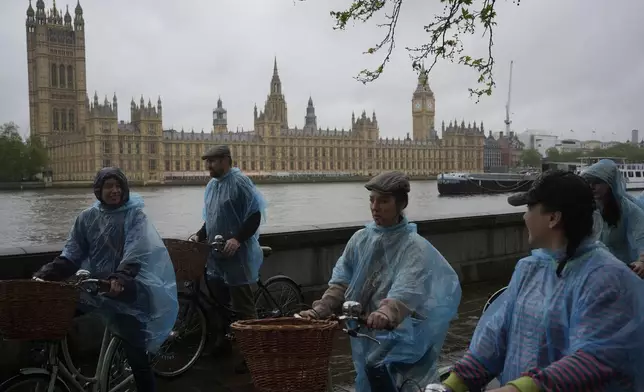 Tourists on a cycle tour in wet weather plastic macs, cycle past the Houses of Parliament, in London Friday, May 3, 2024. Britain's governing Conservative Party is suffering heavy losses as local election results pour in Friday, piling pressure on Prime Minister Rishi Sunak ahead of a U.K. general election in which the main opposition Labour Party appears increasingly likely to return to power after 14 years. (AP Photo/Kin Cheung)
