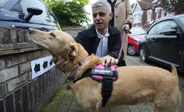 London Mayoral Labour Party candidate Sadiq Khan pats his dog Luna as they pose for the media he arrives to vote in London, Thursday, May 2, 2024. Khan, is seeking re-election, and standing against 12 other candidates for the post of Mayor of London. There are other Mayoral elections in English cities and as well as local council elections. (AP Photo/Kin Cheung)