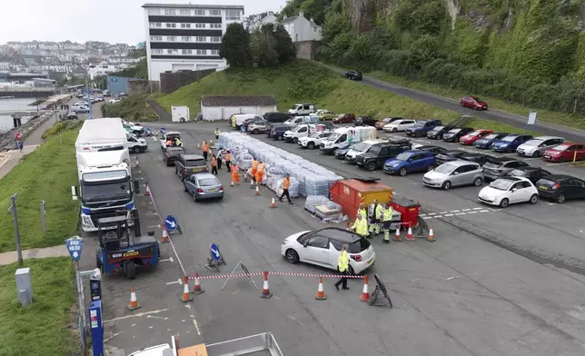 People collect bottled water at Freshwater car park in Brixham, England, Friday May 17, 2024. Around 16,000 households and businesses in the Brixham area of Devon have been told not to use their tap water for drinking without boiling and cooling it first, following the discovery of small traces of a parasite in the local water network. (Ben Birchall/PA via AP)