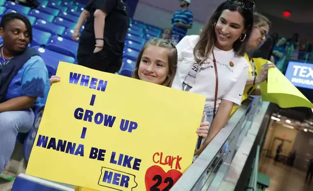 CORRECTS FROM CAITLYN TO CAITLIN - Pailynn Amos, center, holds a sign for Indiana Fever guard Caitlin Clark in front of her mother Rebecca Amos, of Ennis, Texas, prior to an WNBA basketball game against the Dallas Wings in Arlington, Texas, Friday, May 3, 2024. (AP Photo/Michael Ainsworth)
