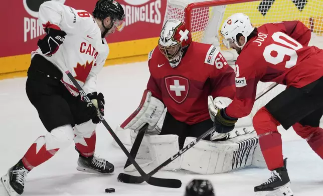 Switzerland's goalkeeper Leonardo Genoni, center, makes a save in front of Canada's Michael Bunting during the semi final match between Canada and Switzerland at the Ice Hockey World Championships in Prague, Czech Republic, Saturday, May 25, 2024. (AP Photo/Darko Vojinovic)