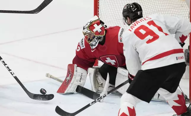 Switzerland's goalkeeper Leonardo Genoni, left, makes a save in front of Canada's John Tavers during the semi final match between Canada and Switzerland at the Ice Hockey World Championships in Prague, Czech Republic, Saturday, May 25, 2024. (AP Photo/Darko Vojinovic)